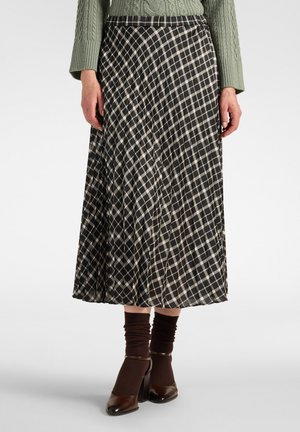 Femme portant une jupe midi plissée à carreaux noir et blanc avec des chaussettes marron, des chaussures marron à talons et un pull vert en maille torsadée.