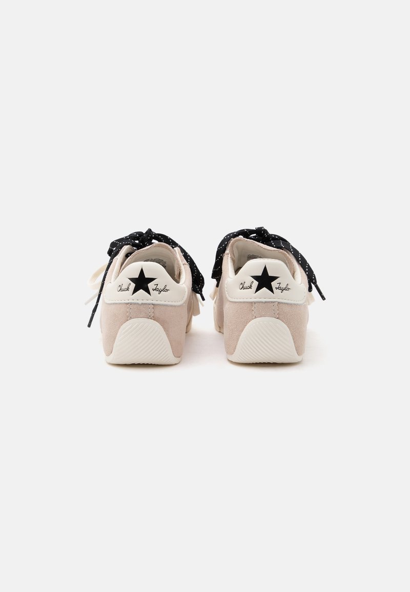 Paar beige Sneakers mit weißen Fersen mit schwarzen Stern-Logos und dem Schriftzug „Chuck Taylor“, schwarze Punkte-Schnürsenkel, die zu Schleifen gebunden sind.