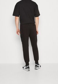 Pantalones de chándal negros con un ajuste slim, que cuentan con bolsillos tipo cargo a los lados y puños acanalados. Combinados con zapatillas negras y grises.