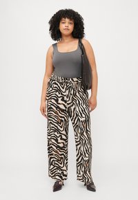 Gray sleeveless top, wide-leg pants with black and beige zebra print. Black bag and pointed black shoes complete the look.