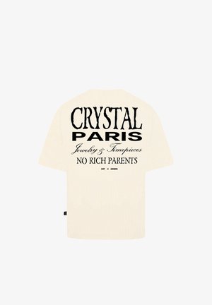 Beige oversize tričko s krátkým rukávem. Na zadní straně je černý potisk s nápisem: "CRYSTAL PARIS Jewelry & Timepieces NO RICH PARENTS."
