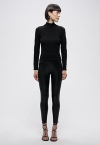 Crni uski rolka iz glatkog, rastezljivog materijala i tajice s visokim strukom od istog glatkog, rastezljivog materijala. Cjelokupni izgled upotpunjuju sandale s remenčićima.