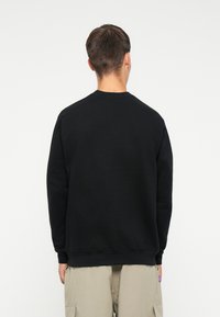 Felpa nera con maniche lunghe e scollo tondo, realizzata in un materiale morbido, caratterizzata da una vestibilità rilassata e polsini a coste.