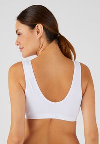 Sujetador inalámbrico blanco con tirantes anchos, espalda redondeada y una textura de tela suave. Diseño minimalista sin hardware visible ni adornos.