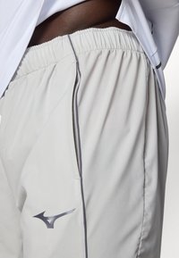 Lichtgrijze sportshorts gemaakt van soepel stof, met een elastische tailleband, zijzakken en een logo aan de onderzijde.
