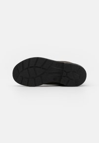 Chaussures brunes avec une semelle en caoutchouc noir texturé, présentant des rainures profondes et des motifs de traction, conçues pour la stabilité et l'adhérence.
