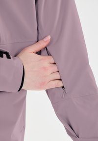 Hihan violetti takin hiha, jossa on vetoketjullinen tasku. Sujuva pinta ja ergonominen muotoilu. Mustat yksityiskohdat hihassa lisäkoristeluna.