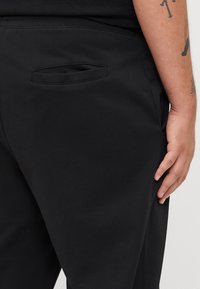 Zwarte joggingbroek van zacht materiaal, met een horizontale zak op de achterkant, een gladde textuur en een elastische tailleband.