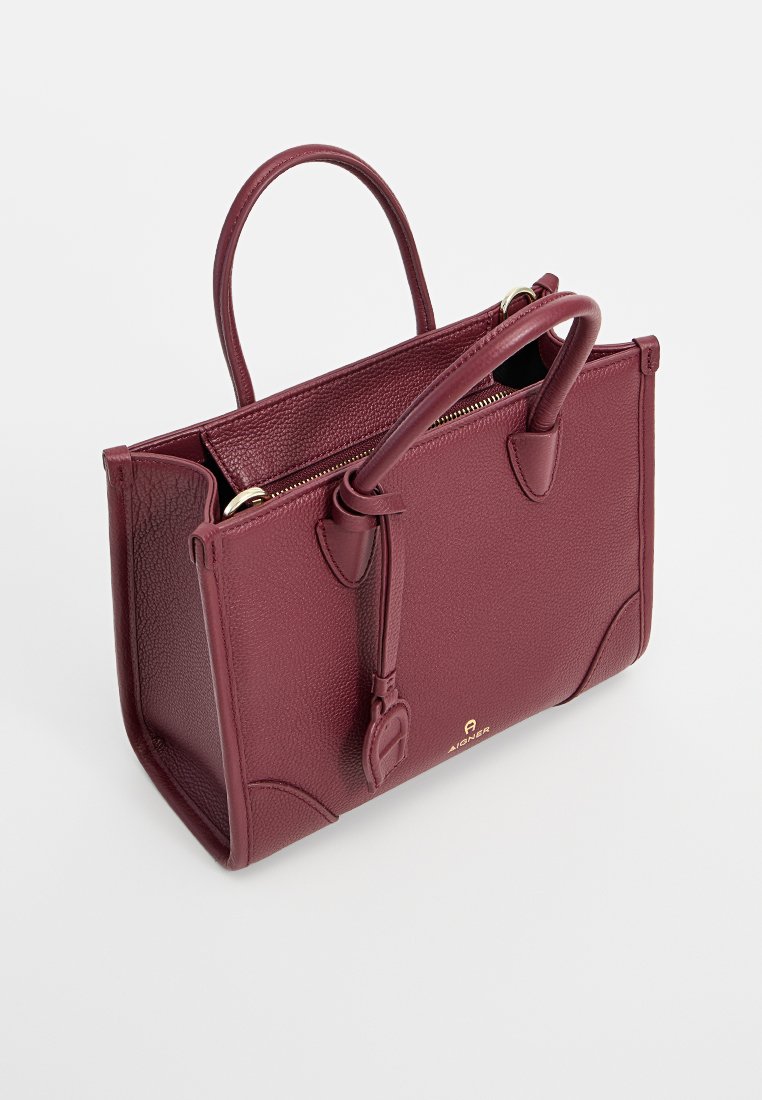 Burgunderfarbene Lederhandtasche mit strukturiertem Finish, doppelten Griffen, Reißverschluss und goldfarbenem Logo-Akzent. Rechteckige Form mit geräumigem Innenraum.
