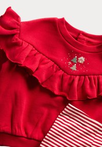 Roter Pullover mit Rüschenausschnitt, verziert mit bestickten Weihnachtsbäumen und Akzenten in Grün und Gold, kombiniert mit rot-weiß gestreiftem Stoff.