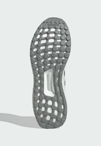 Grå sneakersåle med en teksturert gummioverflate med sirkulære mønstre og en sentral spor. Inkluderer detalj av "Torsjonssystem".