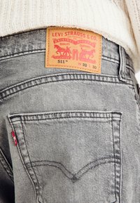 Grå denimjeans med en lærpatch merket "Levi Strauss & Co." og stilnummer 511. Sømmene og detaljene på lommene er synlige.