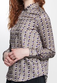 Långärmad blus med knappar i slät, grå satin som har ett upprepande mönster av lila och bruna prickar. Klassisk krage och manschetter med en knapp.