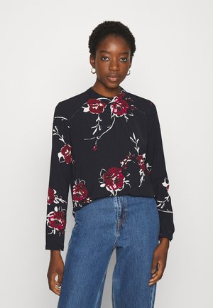 Top de manga longa em azul-marinho escuro com um grande padrão floral branco e vermelho, apresentando um decote redondo e um corte descontraído. Tecido suave, design casual.