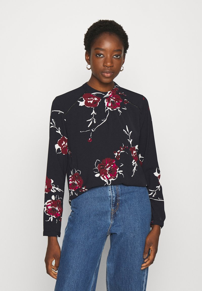 Top de manga longa em azul-marinho escuro com um grande padrão floral branco e vermelho, apresentando um decote redondo e um corte descontraído. Tecido suave, design casual.