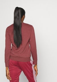 Personne aux longs cheveux noirs attachés en queue de cheval, vue de dos, portant un sweat-shirt bordeaux et un pantalon de survêtement assorti avec des rayures blanches.