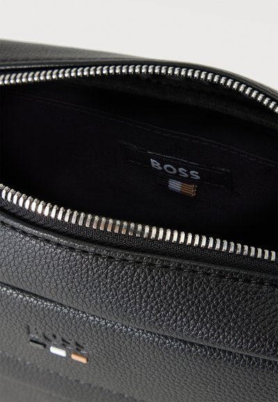 Кадър отблизо на отворена черна чанта Boss от шагренова кожа, със сребрист цип и черна подплата с марката.