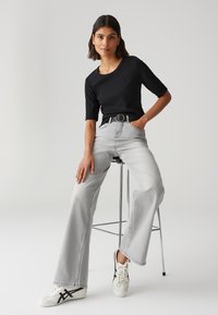 Top corto a righe nere con maniche corte, jeans grigi chiari a vita alta, cintura nera con fibbia tonda, sneakers bianche con dettagli neri.