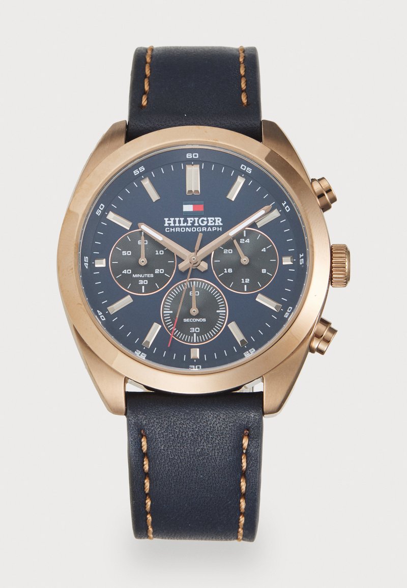 Χρυσό ρολόι χειρός με ναυτικό μπλε καντράν, τρία υποκαντράν, μπεζ δείκτες ωρών και ναυτικό μπλε δερμάτινο λουρί με καφέ ραφές.