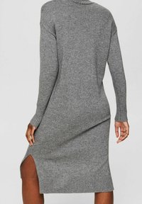 Robe pull grise en maille avec un col haut, des manches longues, des poignets côtelés et une fente latérale. Le tissu a une finition douce et texturée.