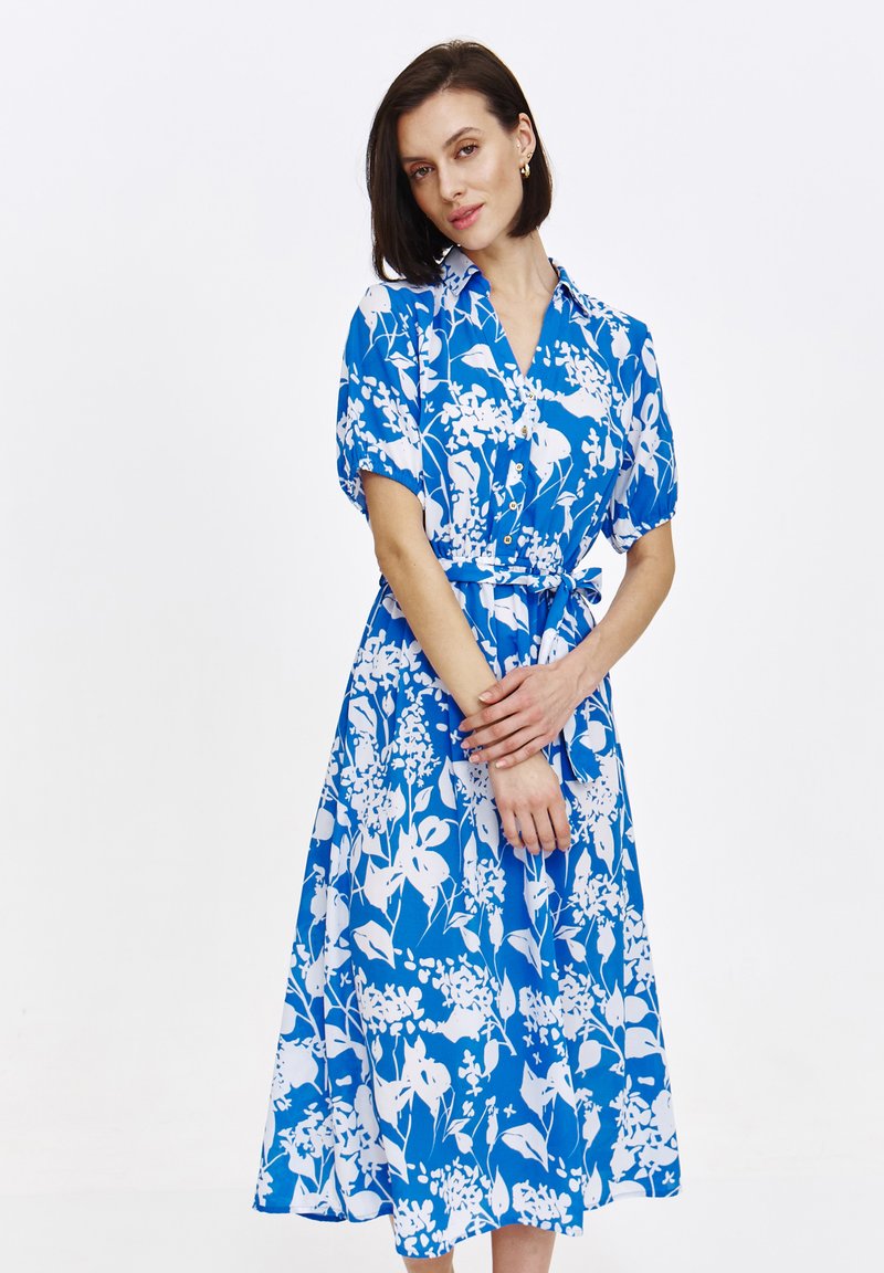 Kwiatowa sukienka w niebieskim kolorze z białymi wzorami, z krótkimi, bufiastymi rękawami, kołnierzykiem i zawiązywanym w pasie dla dopasowanego kroju.