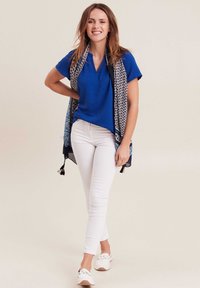 Blauw T-shirt met korte mouwen en een v-hals, gecombineerd met witte slim-fit broeken en een patroon sjaal met franjes. Casual schoeisel.