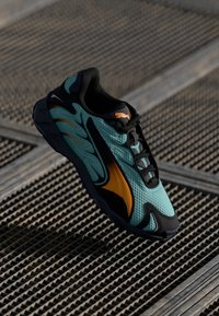 Aqua ja mustad spordijalatsid oranžide detailidega, võrkkangas ülemine osa, kummine tall ja voolujoonis disain õhu läbilaskvuseks. Omab paeltega sulgemist.