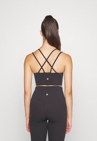Zwarte sportieve crop top met kruislings gesneden banden, gecombineerd met high-waisted leggings. Gladde textuur en logo-detail op de achterkant.