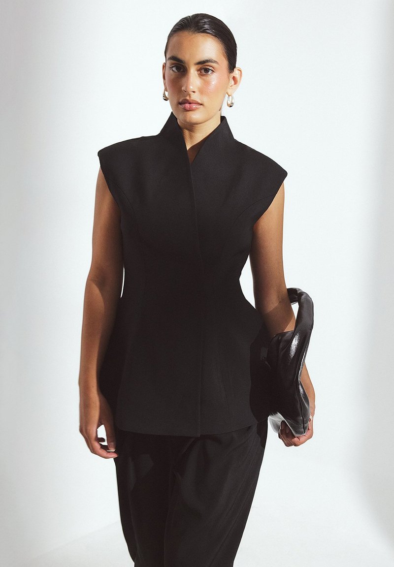 Zwarte gestructureerde top met een hoge kraag en kapmouwen, gecombineerd met losse zwarte broek; gladde stof en minimalistisch ontwerp.
