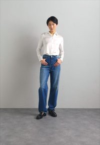 White button-up shirt, high-waisted blue jeans, sleek black shoes, and smooth texture, standing against a light gray background.