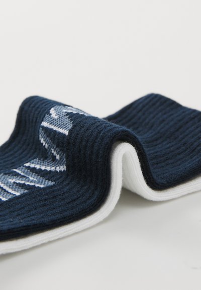 Calcetín azul marino y blanco con textura acanalada. Presenta un patrón de letras blancas en la sección azul marino. Material suave, ligeramente doblado.
