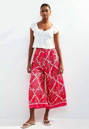 White, textured, short-sleeve blouse with a button at the front, paired with wide, pink floral patterned trousers and flat white sandals.