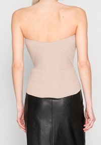 Beige ribbat bandlös topp med en figurnära design, som har vertikala ribbade detaljer och en slät, sömlös finish vid halsringningen och midjan.