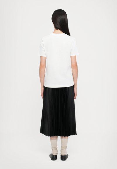 Hvit t-skjorte med korte ermer kombinert med en svart, plissert midi-skirt. Antrekket fullføres med beige knelange sokker og svarte sko med lav hæl.