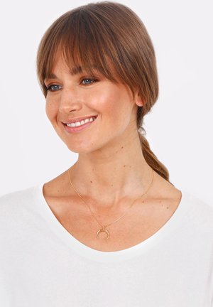 Gold necklace with a crescent moon pendant, fine chain, set against a white shirt. Smooth texture and minimalist design.