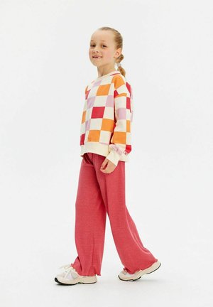 Colorful checkered sweatshirt in orange, pink, and white; paired with loose, pink pants; accented with a soft texture and ribbed cuffs.