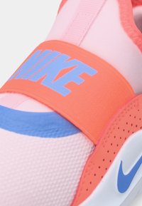 Nike sporta kurpes ar mīksta rozā sieta augšdaļu, oranžu siksnu ar "NIKE" tekstu zilā krāsā, zilu akcentu gar zoli un strukturētām detaļām.