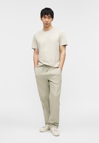 Ανοιχτό μπεζ μπλουζάκι με σχέδια και κοντά μανίκια, συνδυασμένο με φαρδιά, ανοιχτό χακί παντελόνια. Φοριέται με sneakers σε εκρού χρώμα.