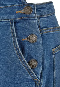 Tissu denim bleu avec une ceinture soigneusement cousue, trois boutons métalliques estampillés "Urban Classics" et un détail de poche latérale.