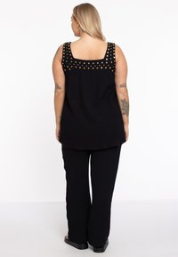 Zwart textuur twee-delige outfit met een mouwloze top met gouden studaccenten op de schouders en wijde broekspijpen.