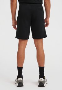 Black cotton shorts with a relaxed fit, visible rear pocket, and stitched hem. Worn with black knee-length socks and gray athletic shoes.