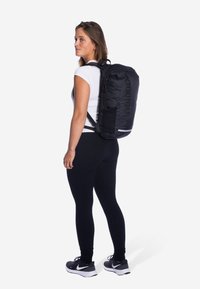 Zwarte rugzak met een slank ontwerp, gemaakt van duurzaam materiaal, met verstelbare schouderbanden, een zijvak en opvallende branding aan de voorkant.