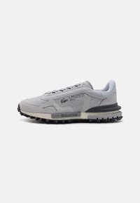 Gray sports shoe with suede and textile upper, featuring a textured rubber sole, lace-up closure, and Lacoste logo on the side.
