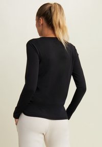 Maglietta nera a maniche lunghe con un design aderente, realizzata in un tessuto morbido, caratterizzata da un collo rotondo e una superficie liscia. Senza motivi visibili.