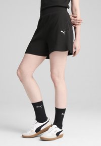 Pantaloni corti neri a coste con vita alta, dotati di un logo Puma bianco sul lato, abbinati a calze nere e scarpe bicolore.