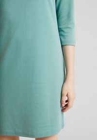 Teall färgad bomullsklänning med 3/4-långa ärmar, lös passform och rund nacke. Slät textur och enkel fålldetalj nertill.