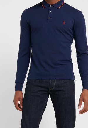 Granatowa koszulka polo z długim rękawem, z kontrastowym kołnierzykiem w paski, listwą z trzema guzikami oraz małym logo na lewej piersi.