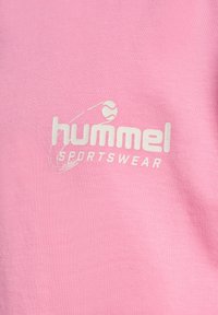 Rosa sportklädesmaterial med en slät textur som har en vit logotyp med texten "hummel SPORTSWEAR" och en svag grafik av en boll.