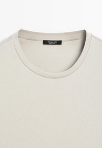 Jasno-beżowa koszulka z okrągłym dekoltem. Gładki bawełniany materiał, krótkie rękawy i metka z napisem "Massimo Dutti" wewn�ątrz.