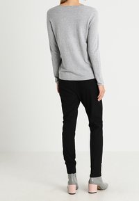 Maglia grigia a maniche lunghe abbinata a pantaloni neri affusolati e stivaletti grigi con tacco rosa. Texture liscia, design semplice e silhouette aderente.